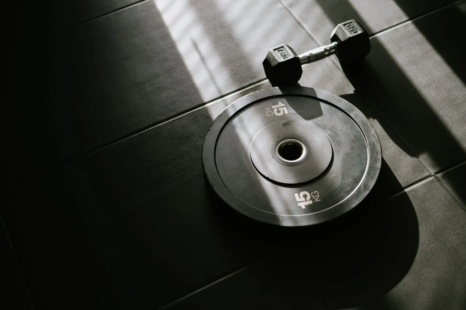 A dumbbell and barbell on a gym floor beside a smartwatch showing a calorie-burn number and a smartphone with a calorie tracking app in a sunlit gym, illustrating how strength-training calories are estimated