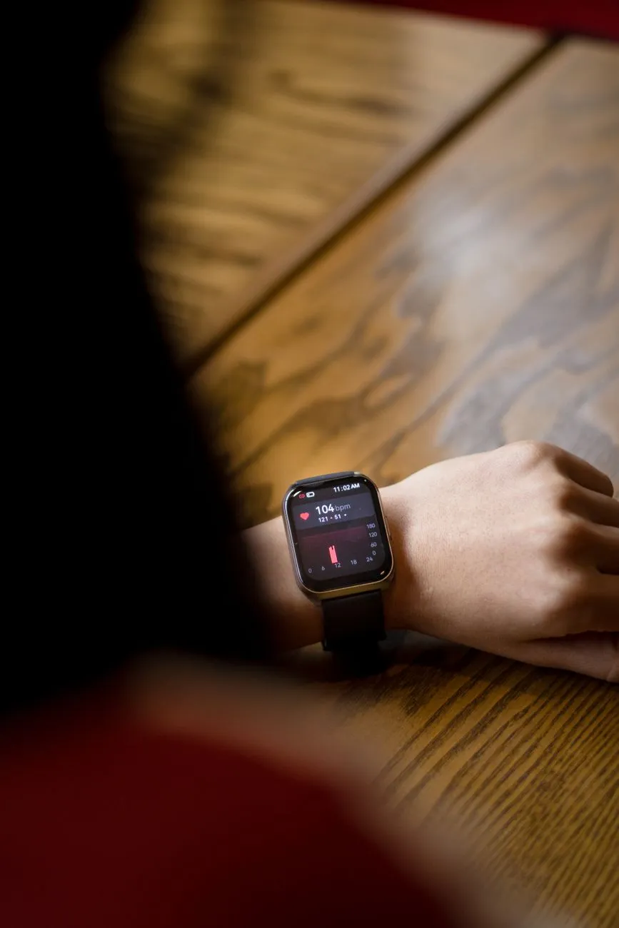 A close-up of a smartwatch on a lifter's wrist during a barbell set beside a chest-strap heart-rate monitor, illustrating why wrist trackers estimate lifting calories poorly
