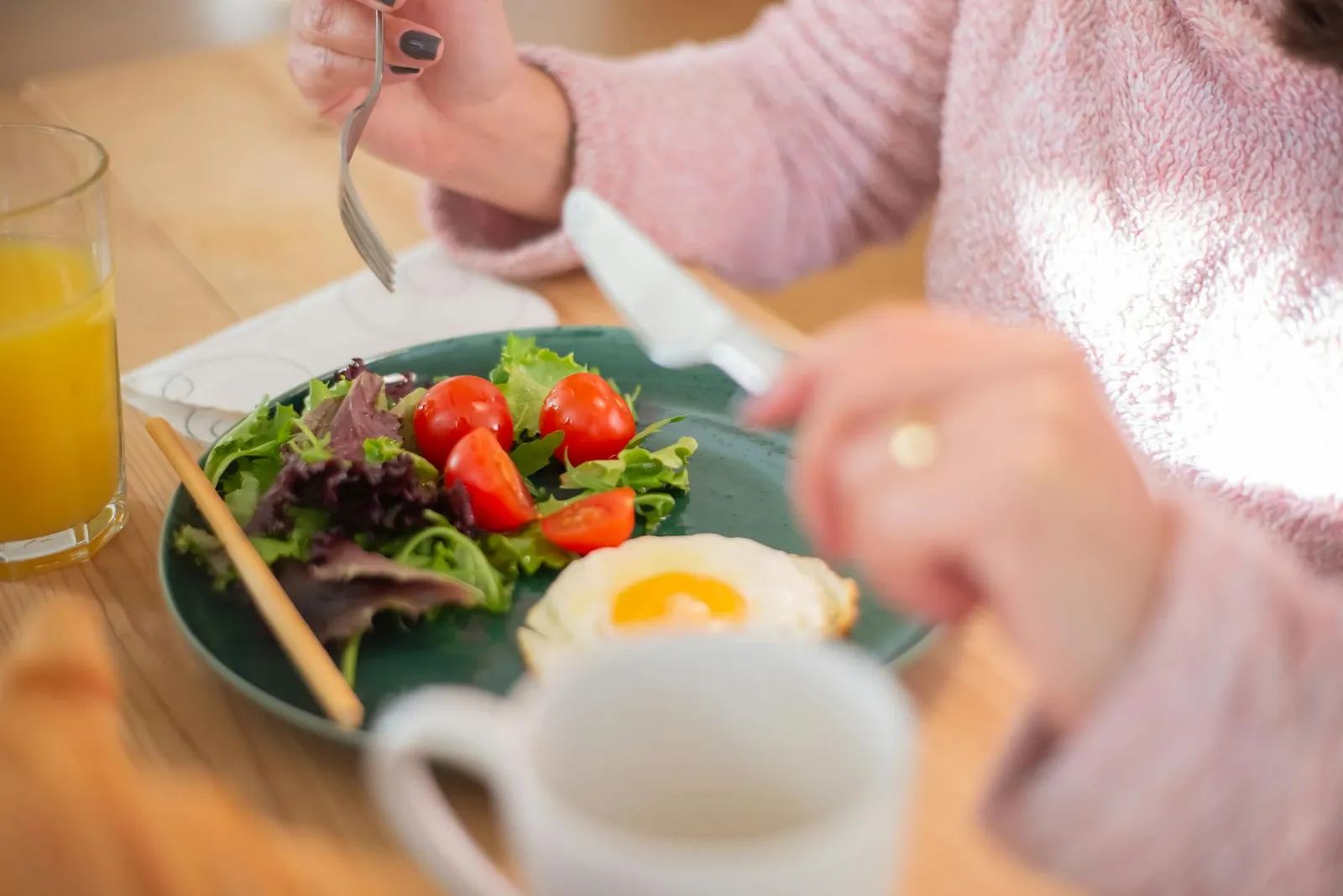 Person enjoying a balanced healthy meal at a sunlit kitchen table with fresh produce and a glass of water