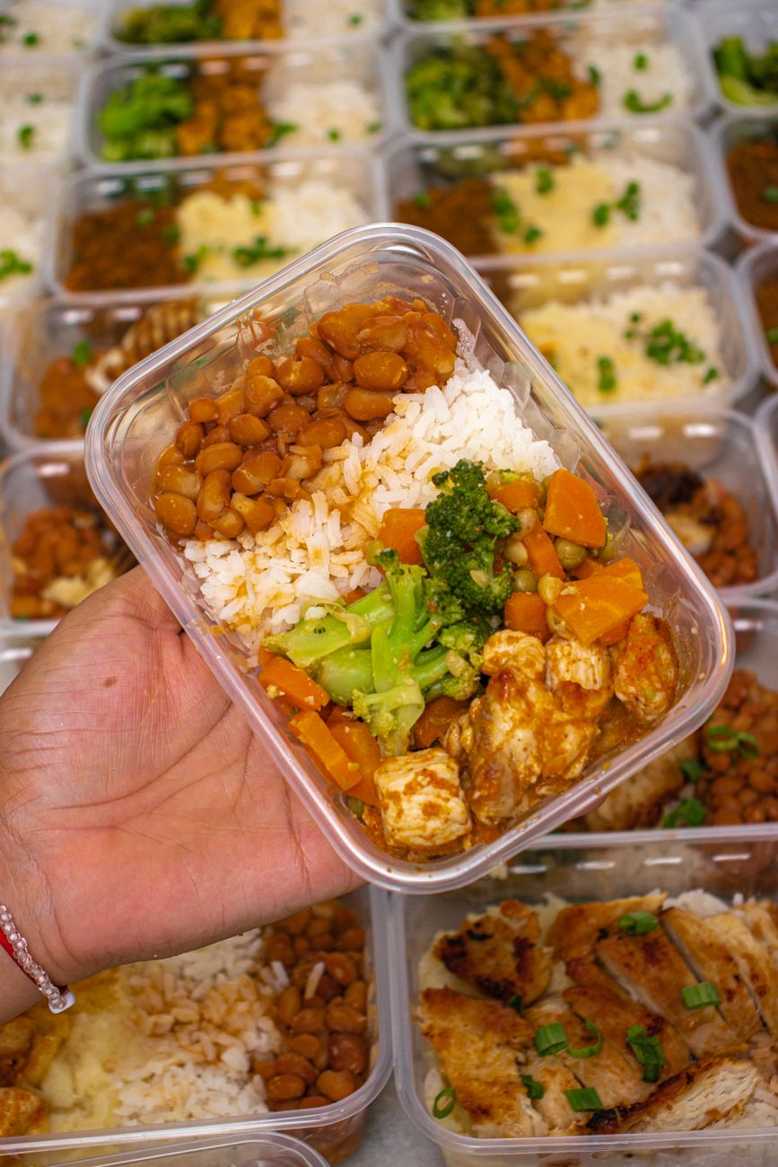 A calculator and an open notebook with a worked thermic-effect-of-food calculation beside meal-prep containers of chicken, rice, and vegetables on a sunlit kitchen counter, illustrating the net-calorie math for a 2,000 kcal day