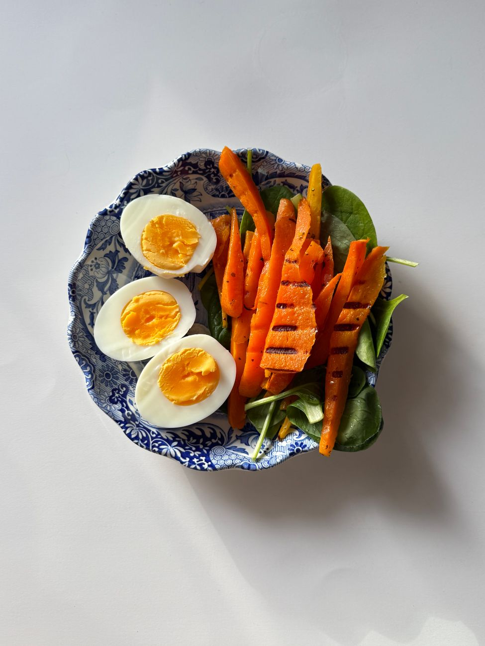Grilled salmon, boiled eggs, and a bowl of Greek yoghurt beside a food diary and a smartphone showing a calorie tracking app in a sunlit kitchen, illustrating the modest daily calorie advantage of a higher-protein split