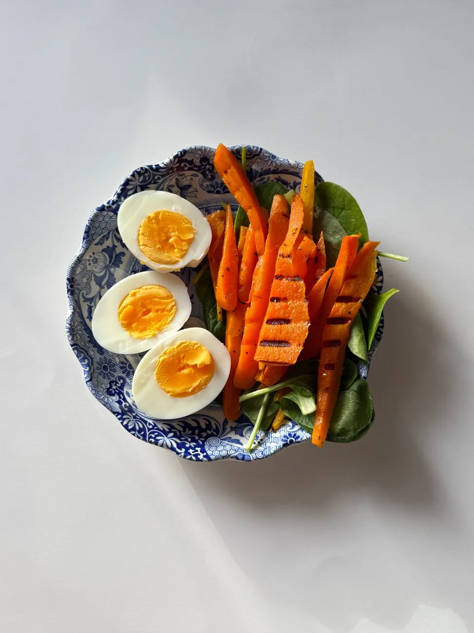 Grilled salmon, boiled eggs, and a bowl of Greek yoghurt beside a food diary and a smartphone showing a calorie tracking app in a sunlit kitchen, illustrating the modest daily calorie advantage of a higher-protein split