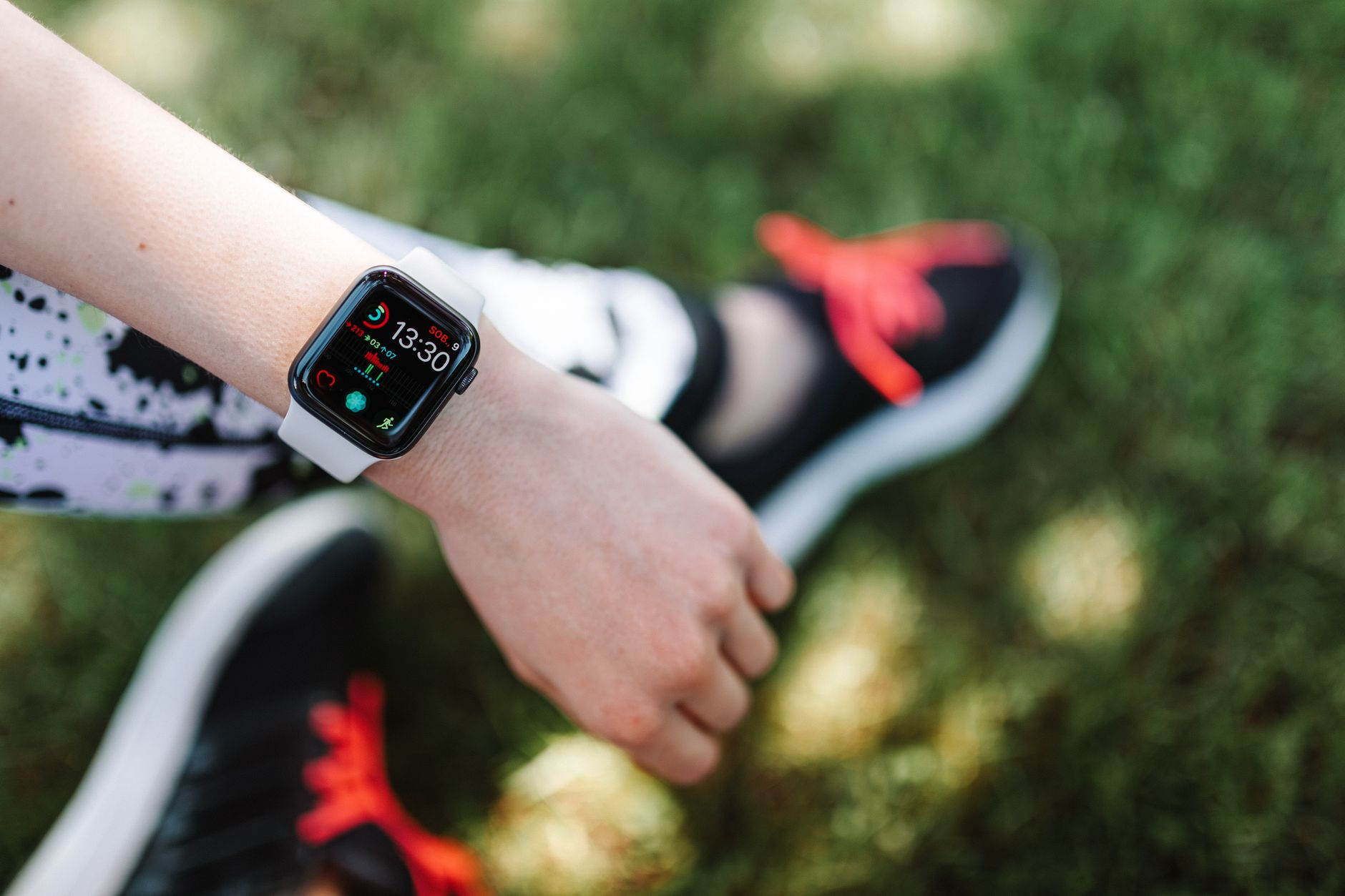 Walking shoes on a sunlit park path beside a smartwatch displaying step count and pace on a wooden bench