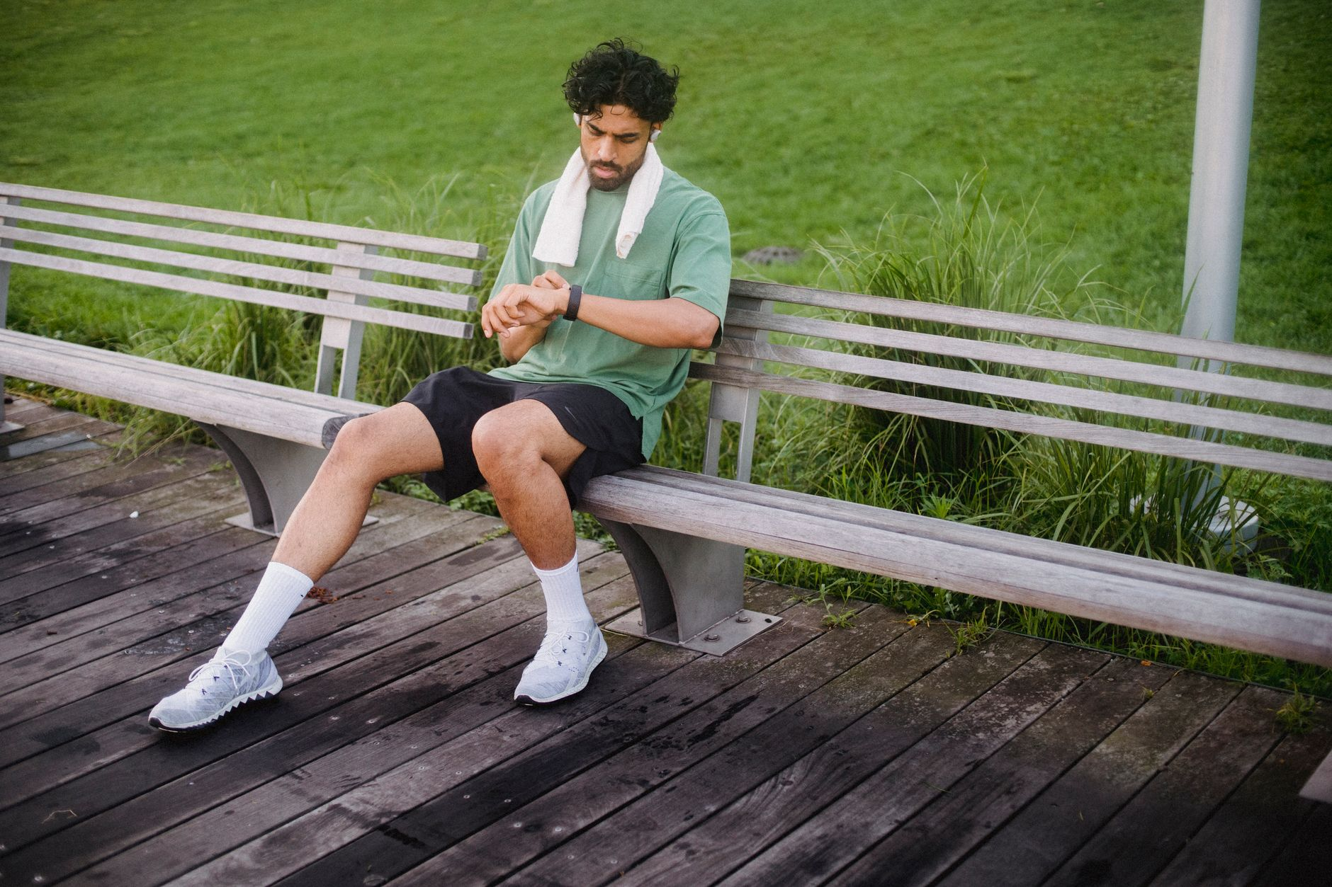 A pair of walking shoes on a sunlit park path beside a smartwatch showing step count and a printed walking calorie chart on a wooden bench
